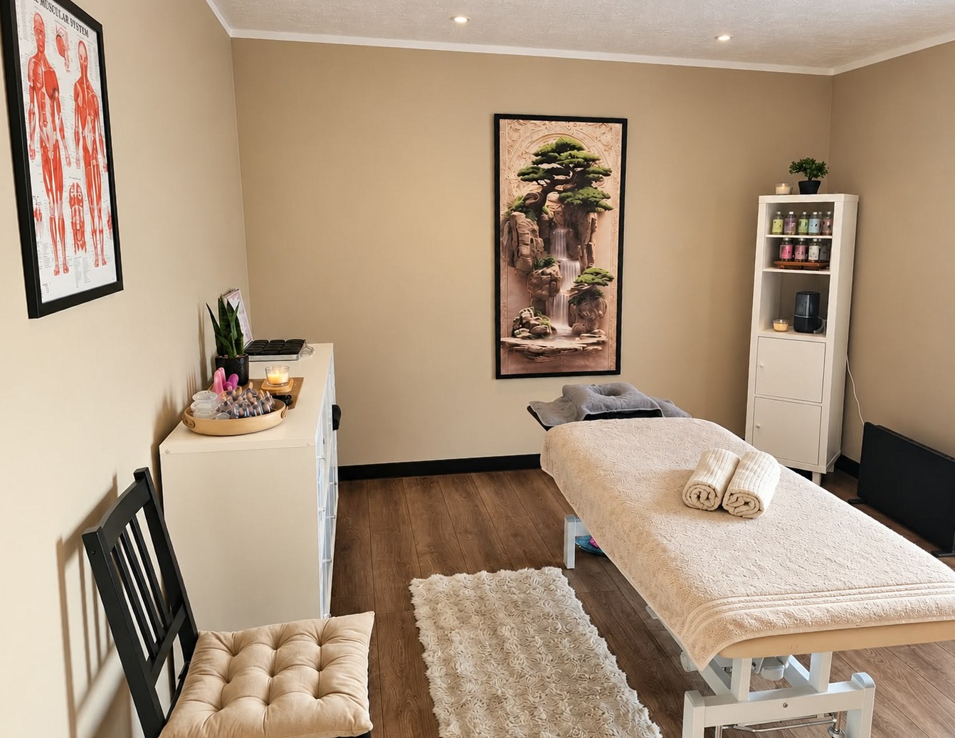 De behandelkamer van Calma tu mente met massagetafel, opgerolde handdoeken en een schilderij met een bonsai